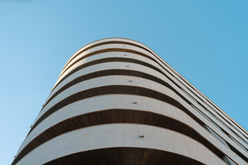 Low-angle view of a modern curved building with horizontal lines. The sleek design and...