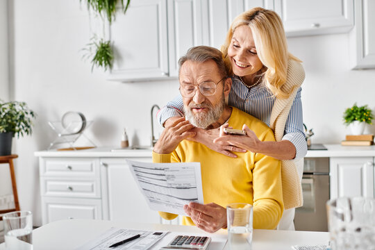 A mature loving couple in cozy homewear examining a mysterious piece of paper in their kitchen at home. - Powered by Adobe