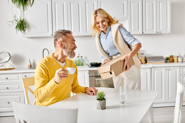 Fototapeta premium A mature man and woman in cozy homewear are seen moving boxes into a kitchen together at home.