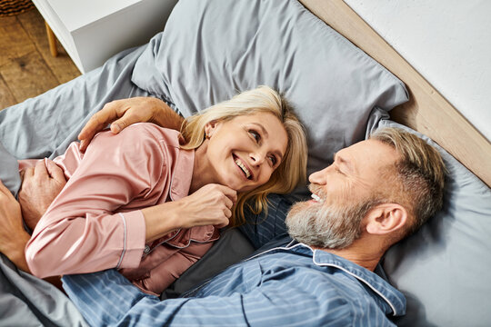 A mature loving couple in cozy homewear laying together on a bed, sharing a peaceful moment of intimacy and connection.