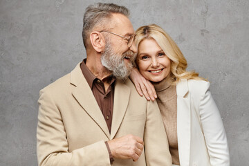 A mature man and woman in stylish attire stand closely together, exuding elegance and affection...