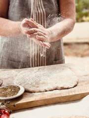 Woman baker with flour in her hands and homemade pizza dough on the table.