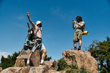 A young gay couple celebrates reaching a mountain peak during a summer hike.