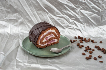 Chocolate roll with cheese and forest fruits filling and coffee beans on a ceramic plate, on silver cloth background