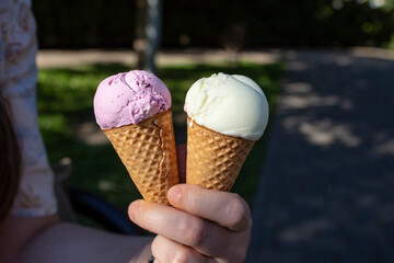 Woman hand holding two ice cream cones on defocused dark park background, soft focus close up