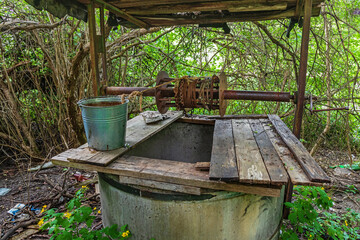 Obraz premium Old well in the forest. Rusty bucket at a water source in the countryside