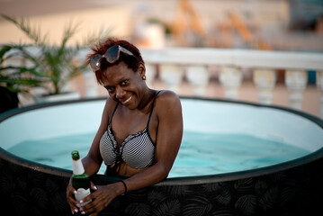 African Woman relaxes in a hot tub and drinks from a bottle of beer on the hotel terrace. Relax in the summer heat with a cool drink