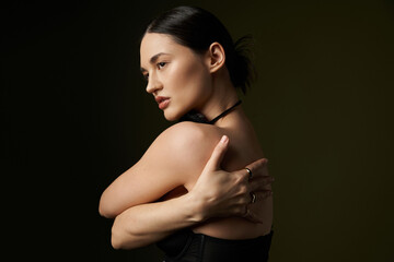 Fototapeta premium A young woman with dark hair and a flower choker poses against a black background.