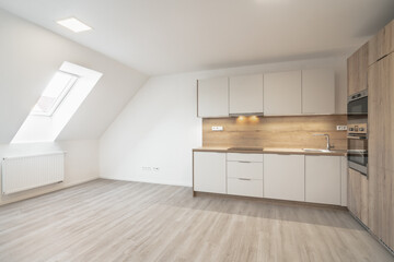 Bright attic kitchen with modern cabinets, wood accents, and ample natural light from a skylight window. Sleek countertops, built-in appliances, and a spacious, open layout enhance the design.