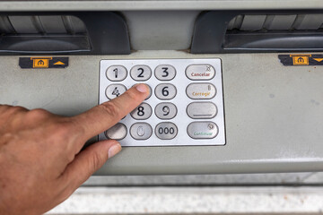 A person pressing the numbers on a keypad located on a public machine interface, possibly an ATM or ticket machine, symbolizing secure transactions and digital interaction.