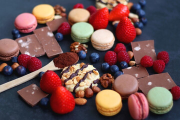 Macarons, chocolate, cookies, berries and various nuts on dark blue background. Selective focus.