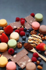 Macarons, chocolate, cookies, berries and various nuts on dark blue background. Selective focus.