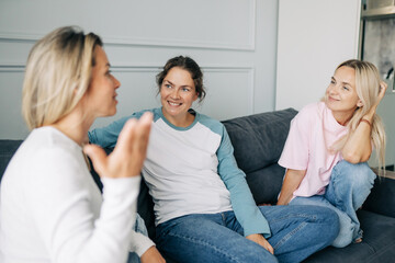 Three girlfriends chatting happily while sitting on the couch at home. Discussion of private life and social issues.