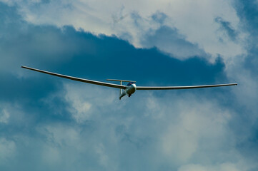 A white glider is soaring through the cloudy sky.