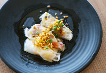 Close up  Streamed Chinese noodle rolls on black dish with natural light, close up food streamed Chinese noodle rolls topping with deep fried garlics and spring onions.