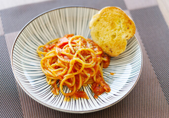 Close up small portion of spaghetti bolognese with baked bread in a beautiful dish with natural light.