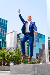Young redhead businessman jumping joyfully in modern business park.