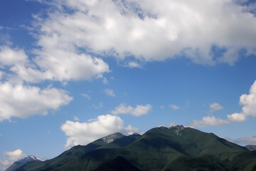 Fototapeta premium Mountains in nature with blue sky. Mountain travel green concept. Clouds in the sky over mountains in nature. Mountains and clouds in a blue sky lifestyle with nature.
