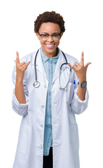 Fototapeta premium Young african american doctor woman wearing medical coat over isolated background shouting with crazy expression doing rock symbol with hands up. Music star. Heavy concept.