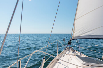 Fototapeta premium White sloop rigged yacht sailing at sunset. Clear sky after the storm. View from the deck to the bow, mast, sails. Transportation, travel, cruise, sport, recreation, leisure activity, racing