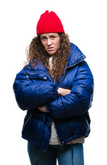Beautiful young brunette curly hair girl wearing winter coat, wool cap and sweater over isolated background skeptic and nervous, disapproving expression on face with crossed arms. Negative person.