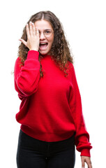 Beautiful brunette curly hair young girl wearing glasses and winter sweater over isolated background covering one eye with hand with confident smile on face and surprise emotion.