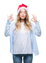 Beautiful young blonde woman wearing christmas hat over isolated background relax and smiling with eyes closed doing meditation gesture with fingers. Yoga concept.