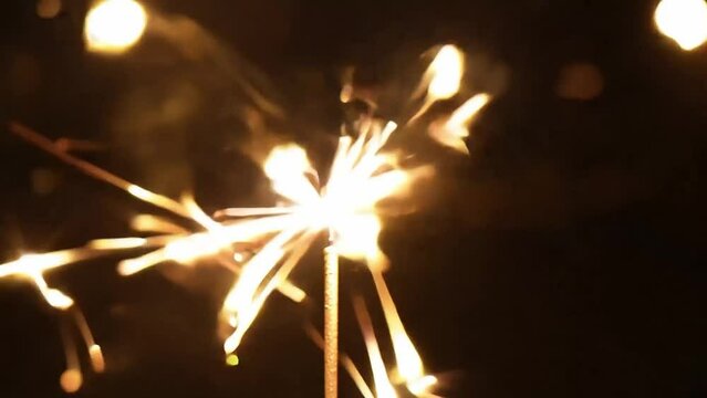 Slow motion close up of a sparkler that lights up function sparks against a black background.