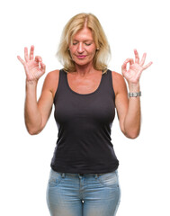 Fototapeta premium Middle age blonde woman over isolated background relax and smiling with eyes closed doing meditation gesture with fingers. Yoga concept.