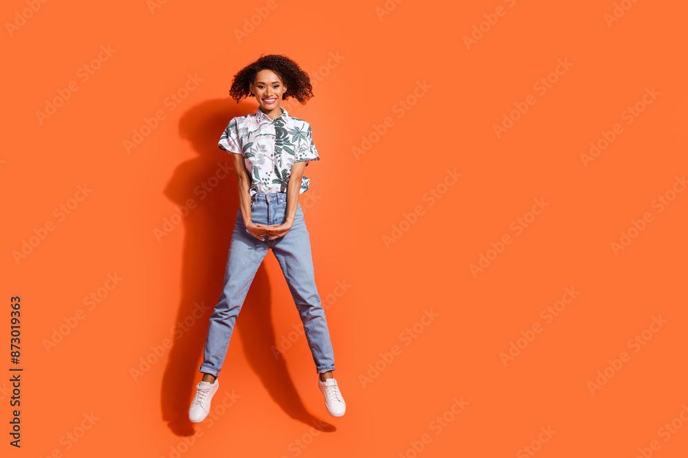 Wall mural Full body length photo of american woman in jeans and summer stylish shirt jumping up gymnastics isolated on orange color background