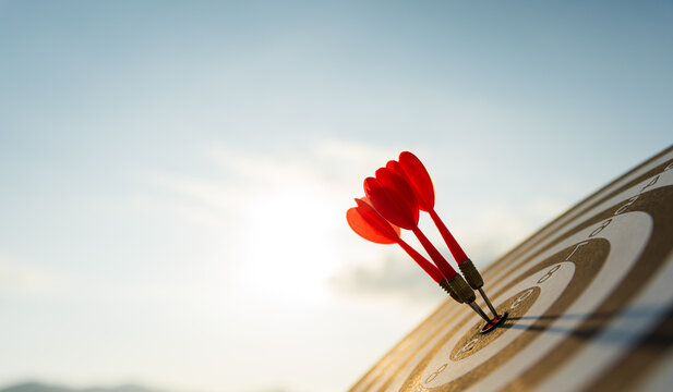 Close up shot red darts arrows in the target center on dark blue sky background. Business target or goal success and winner concept.