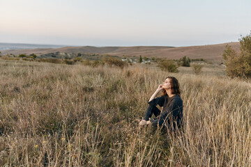 Woman relaxing in tall grass on hill during sunset in field