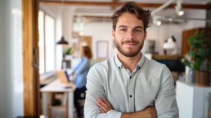 Obraz premium A smiling man with a beard stands confidently with crossed arms in a modern office space, embodying professionalism and a welcoming, collaborative work environment.