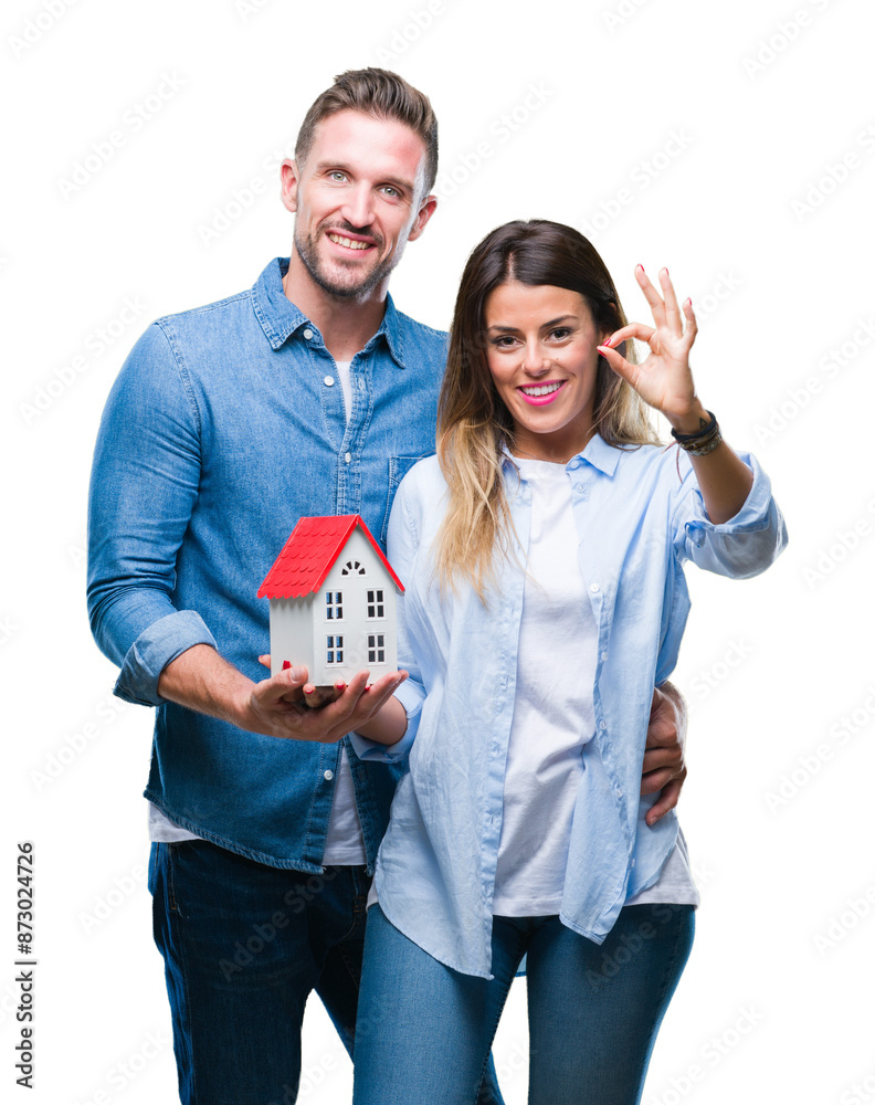 Sticker Young couple in love holding house over isolated background doing ok sign with fingers, excellent symbol