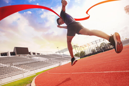 Fit young man running sprinting to red finish line at the racetrack. Finisher, marathon runner sprinting moment at the racetrack.
