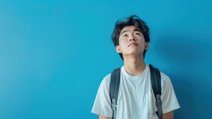 Contemplative Asian Student Posing Against Blue Background with Copy Space for Text