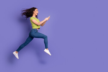 Full size photo of pretty teen girl hold gadget running wear trendy green outfit isolated on purple color background