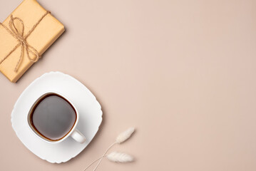 Cup of coffee with gift box on beige background from above. Flat lay, top view. Copy space