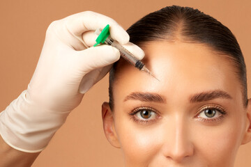 Cosmetologist doctor making botox injection in forehead to young European woman, lady getting...