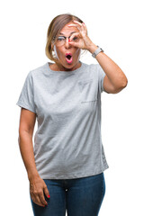 Middle age senior hispanic woman wearing glasses over isolated background doing ok gesture shocked with surprised face, eye looking through fingers. Unbelieving expression.