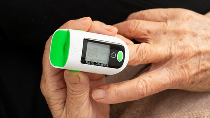 Elderly woman checking fingertip pulse oximeter oxygen meter blood monitor