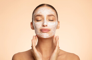 Young European lady posing with facial mask and closed eyes, enjoying beauty skincare treatments,...