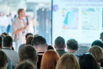 Speaker giving a presentation to a large audience during a conference or seminar, with attendees listening attentively.