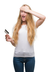 Naklejka premium Blonde teenager woman holding credit card stressed with hand on head, shocked with shame and surprise face, angry and frustrated. Fear and upset for mistake.