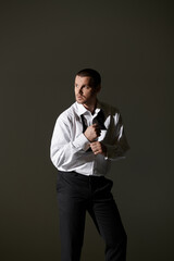 Man adjusts bowtie dramatically against gray background.