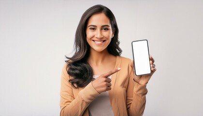 A young modern happy Indian Asian woman or female is showing and pointing a finger at a mobile phone or smartphone blank screen and smiling looking at the camera isolated on a white background.
