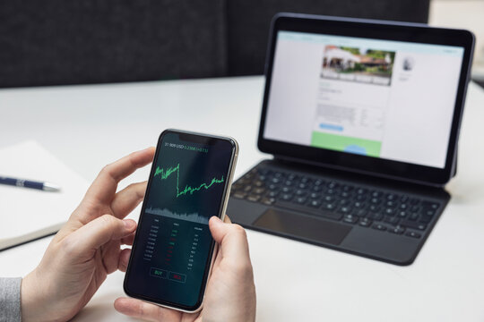 Cropped hands of businesswoman analyzing graph on smart phone against laptop on desk at office