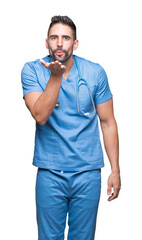 Handsome young doctor surgeon man over isolated background looking at the camera blowing a kiss with hand on air being lovely and sexy. Love expression.