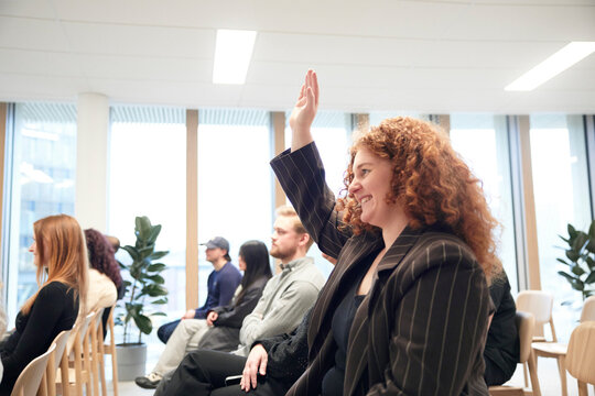 Smiling young businesswoman raising hand during meeting in office