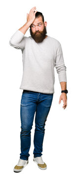 Young blond man wearing casual sweater surprised with hand on head for mistake, remember error. Forgot, bad memory concept.